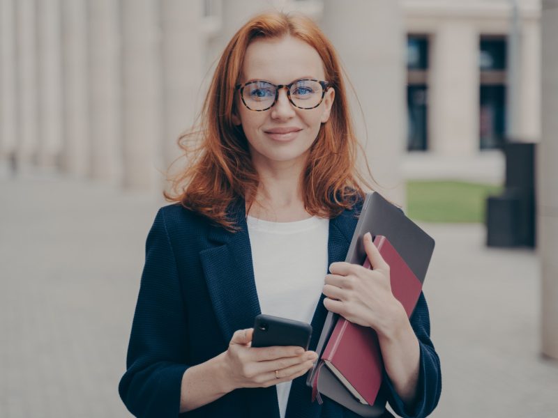 confident-beautiful-red-haired-female-business-consultant-holding-modern-smartphone-and-laptop.jpg